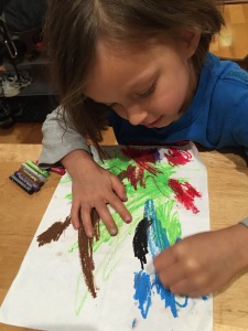 preschool-aged boy colors with oil pastels